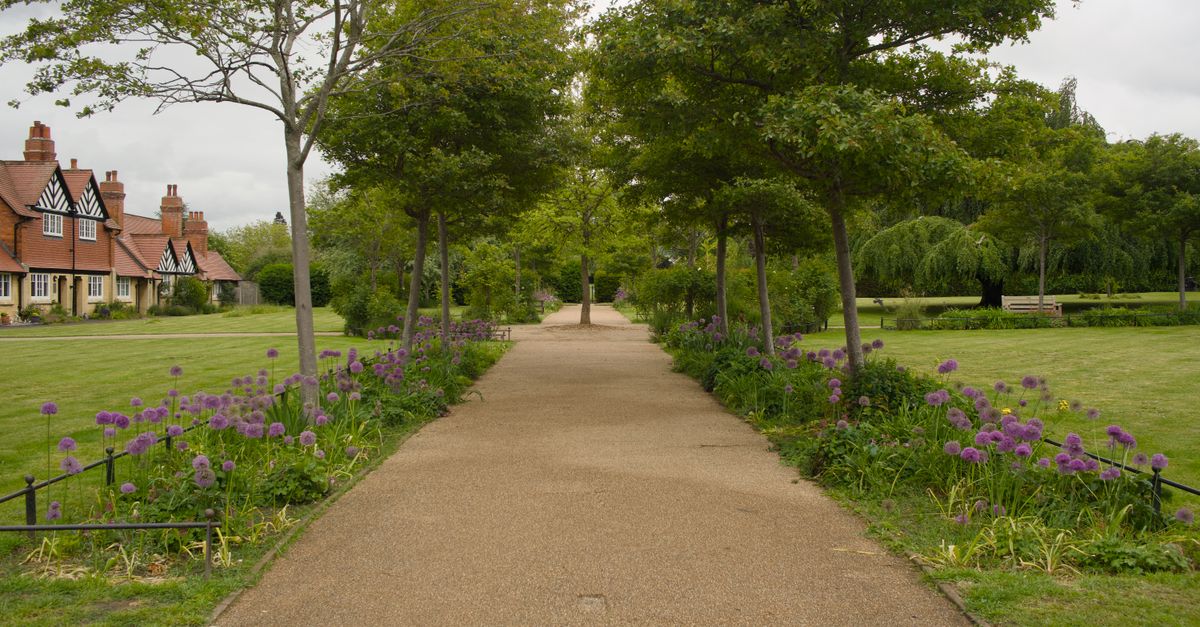 A picturesque pathway lined with trees and purple flowers in Cheltenham, England.