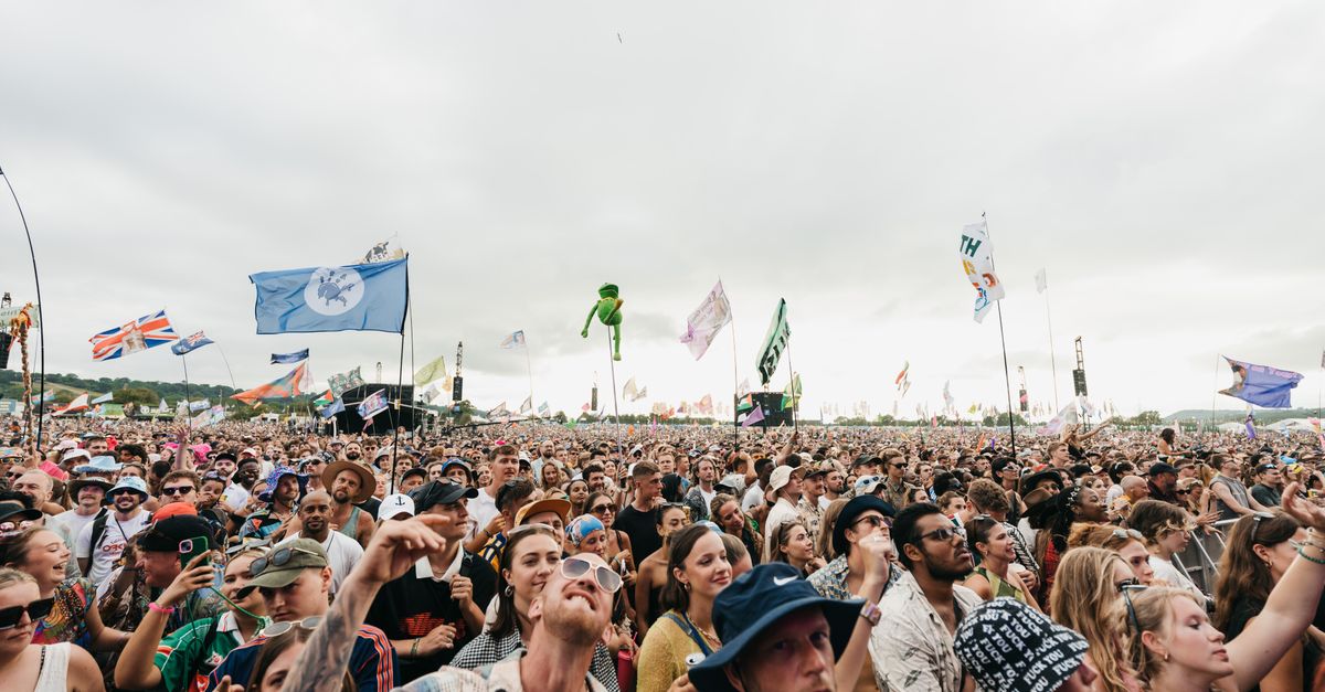 A lively crowd enjoying the Glastonbury Festival in England, with flags waving across the sky.