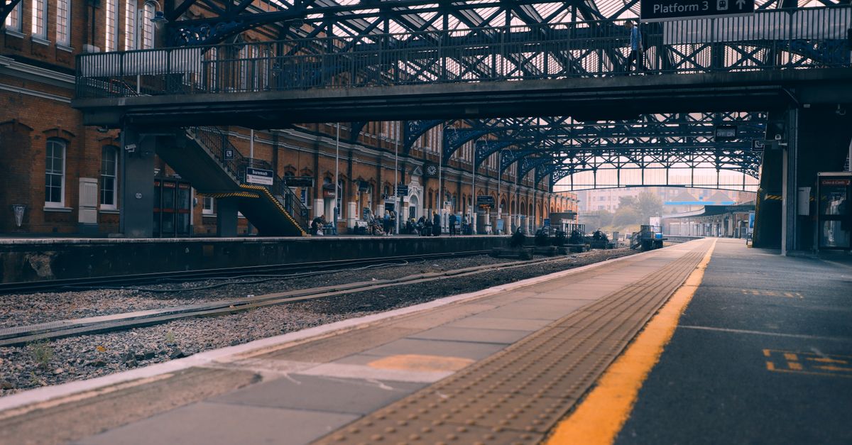 Victorian-era UK railway station platform with overhead footbridge and 'Platform 3' sign