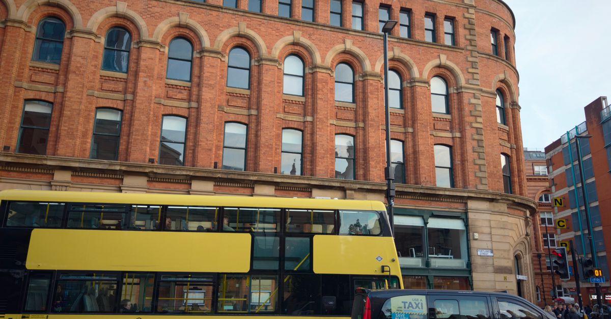 City street scene with yellow bus and taxi in front of historic brick building.