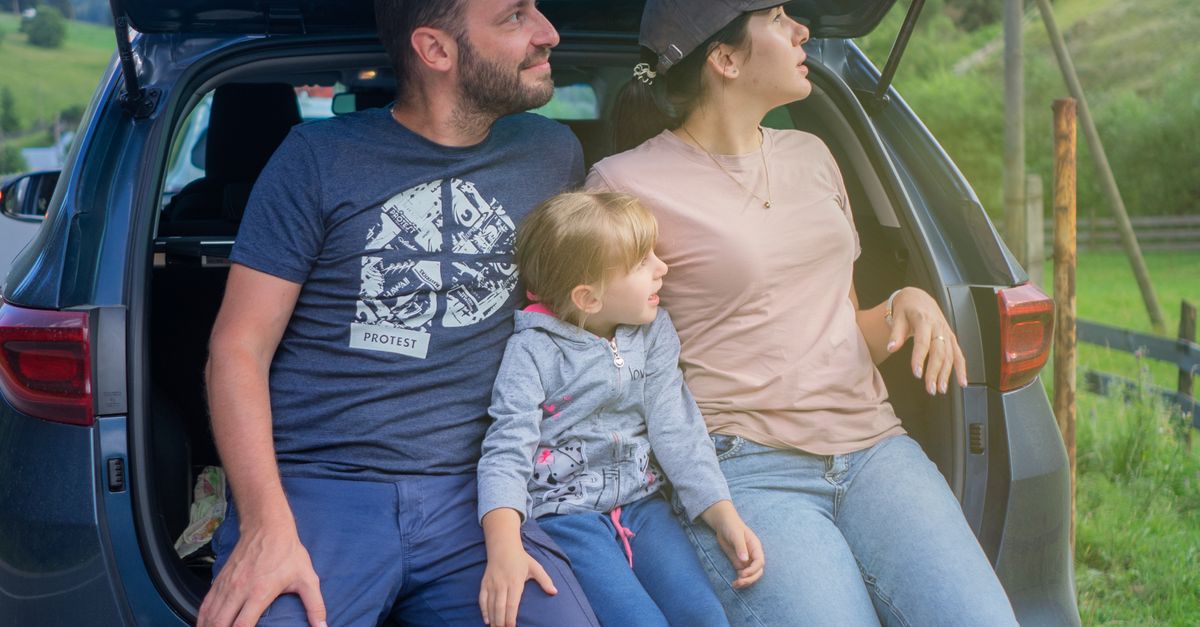 A family sits in a car trunk, enjoying an outdoor adventure in a scenic countryside.