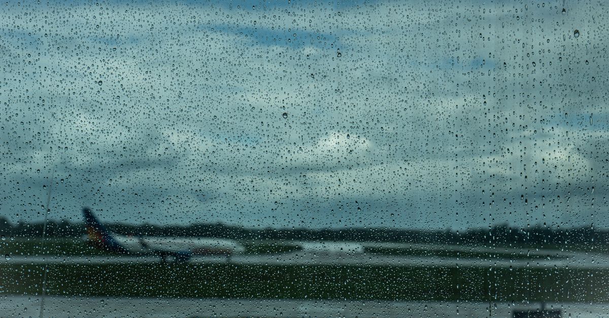 Airplane in the distance through raindrop-covered window at airport.