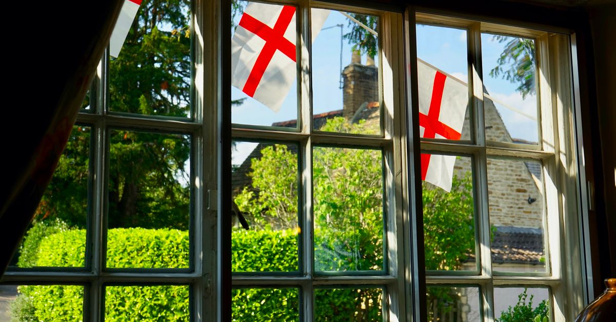 Quaint English cottage view through window with England flags outside, lush greenery visible.