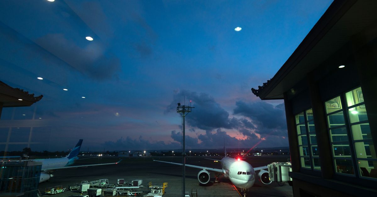 Contemporary airplanes with red beacon parked on airfield near airport service vehicles and terminal at night