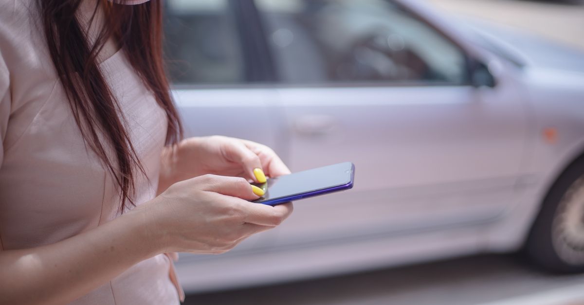 Close-up of a woman checking her phone next to a parked car while waiting for her ride