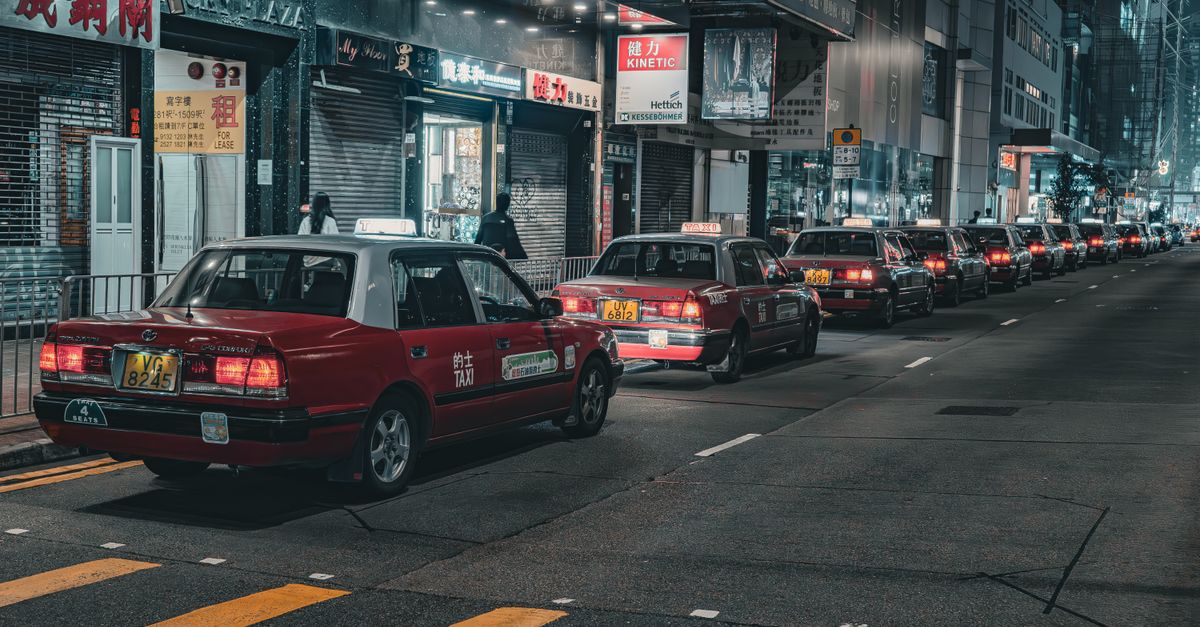 A street in Hong Kong bustling with red taxis at night, capturing urban life and city lights.